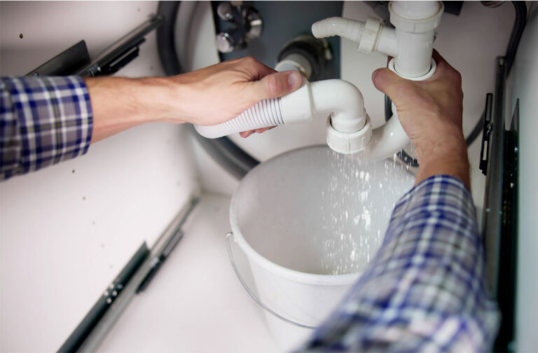 Plombier démontant un siphon sous un évier, l'eau coule dans un seau.